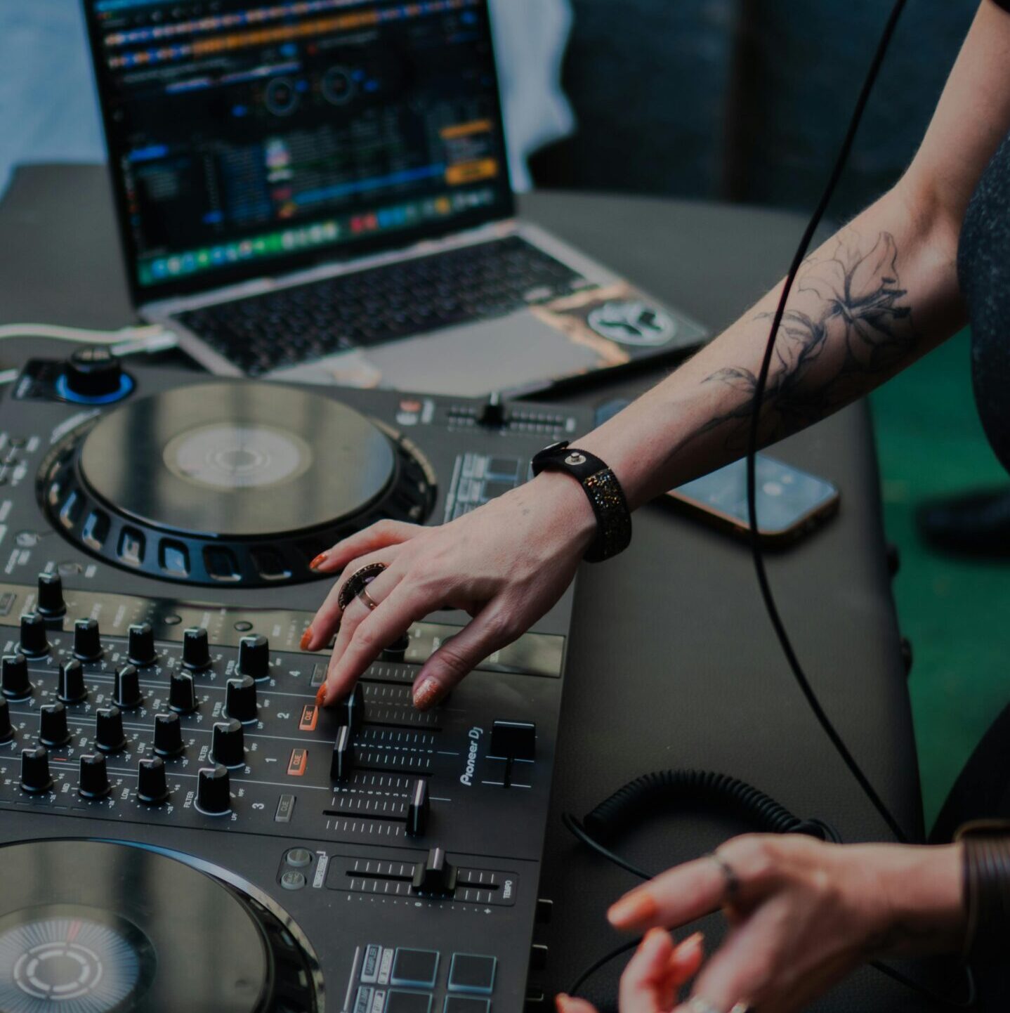 DJ manipulating audio mixer and laptop for live performance at indoor event.